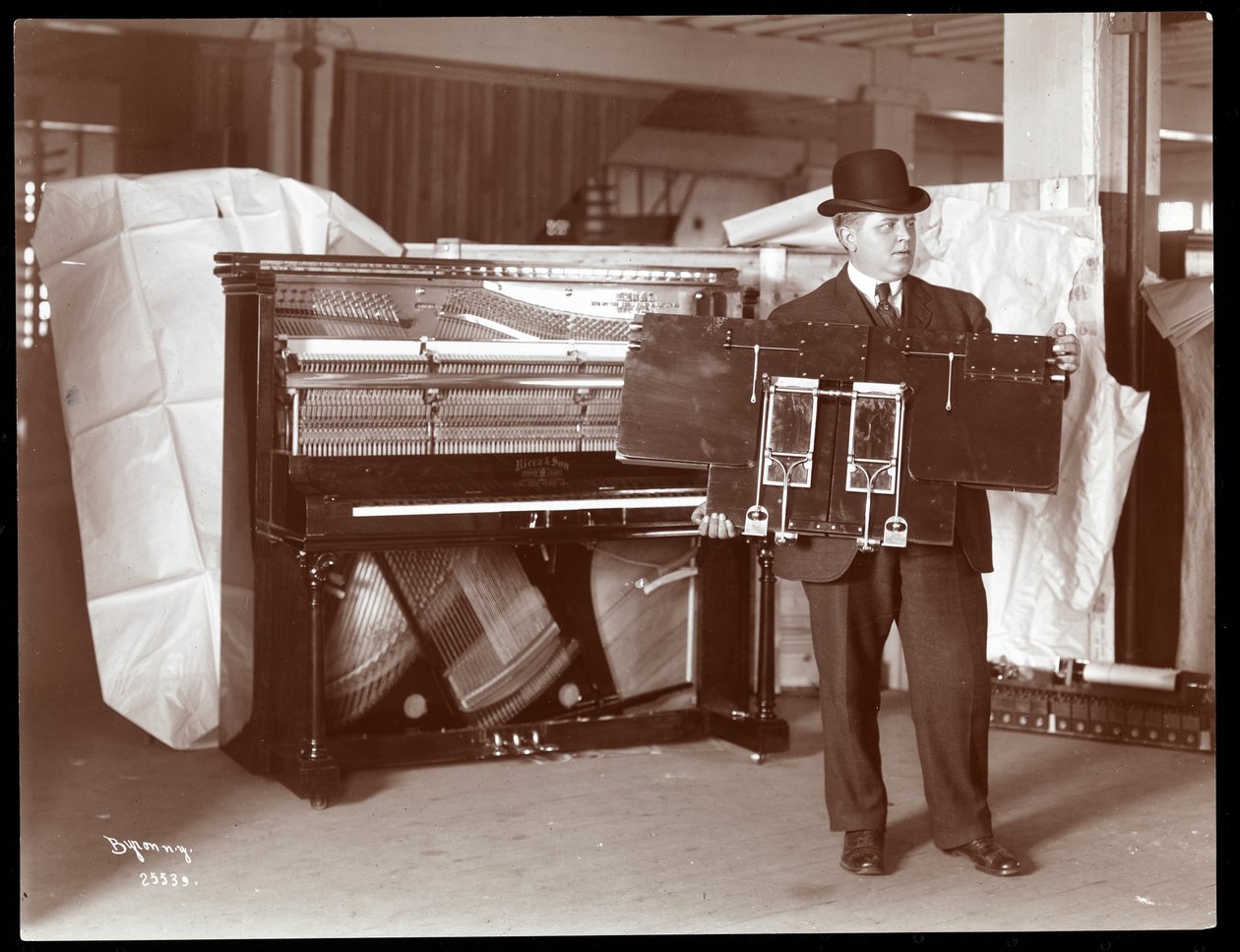 Un piano par Ricca und Son Piano Co. avec un homme tenant une partie des mécanismes du piano, 1907 - Byron Company