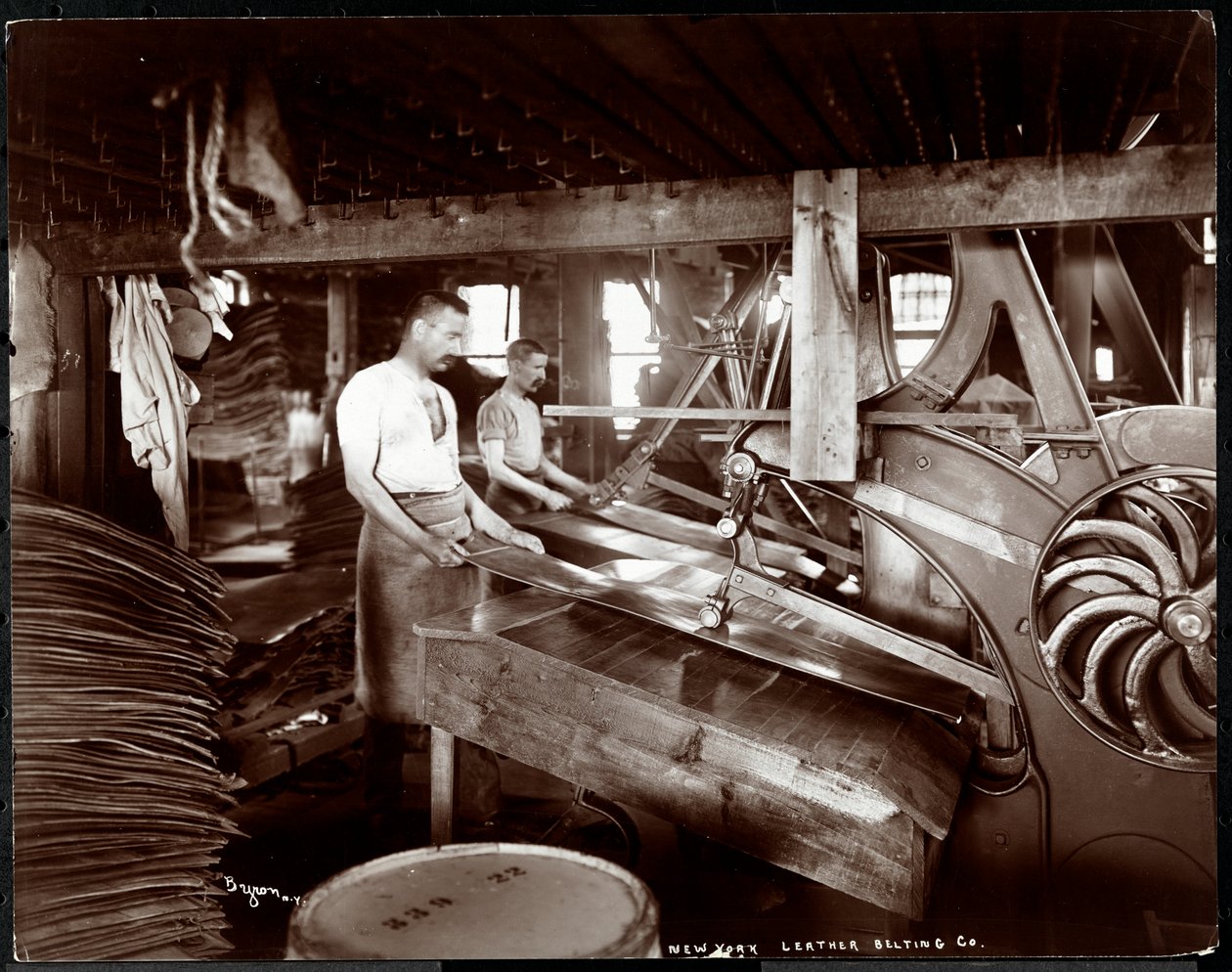 Vue intérieure de deux hommes travaillant avec du cuir et des équipements lourds à la New York Leather Belting Co., New York, 1905 - Byron Company