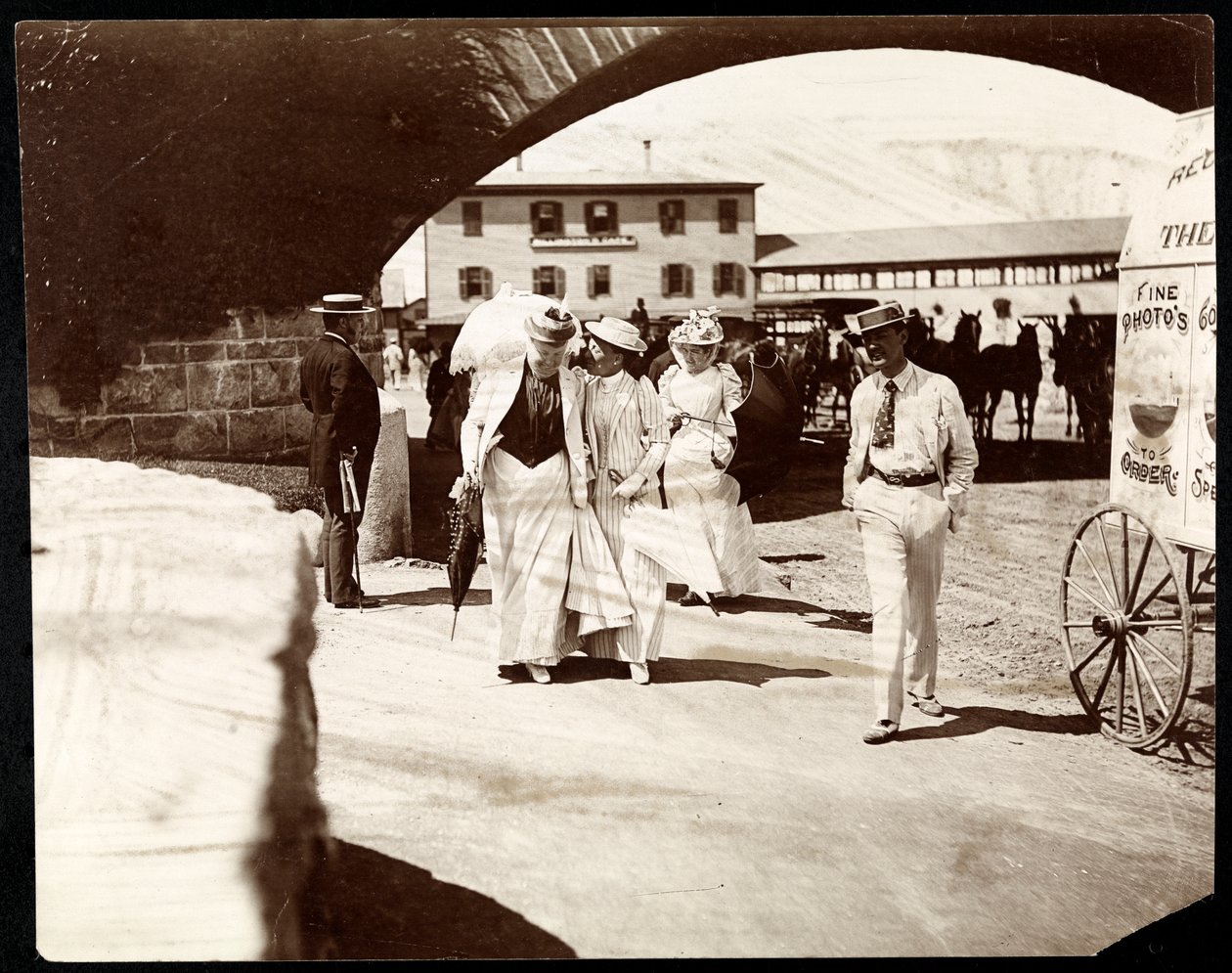 Trois femmes et un homme marchant au Narragansett Pier avec le chariot du photographe itinérant, Rhode Island, 1891 - Byron Company