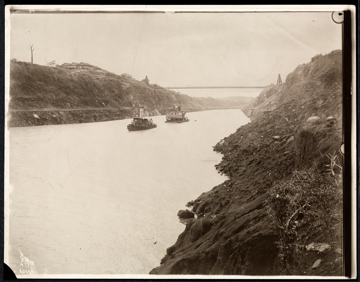 Vue de deux bateaux dans le canal de Panama pendant sa construction avec un pont suspendu au-delà, 1913 - Byron Company