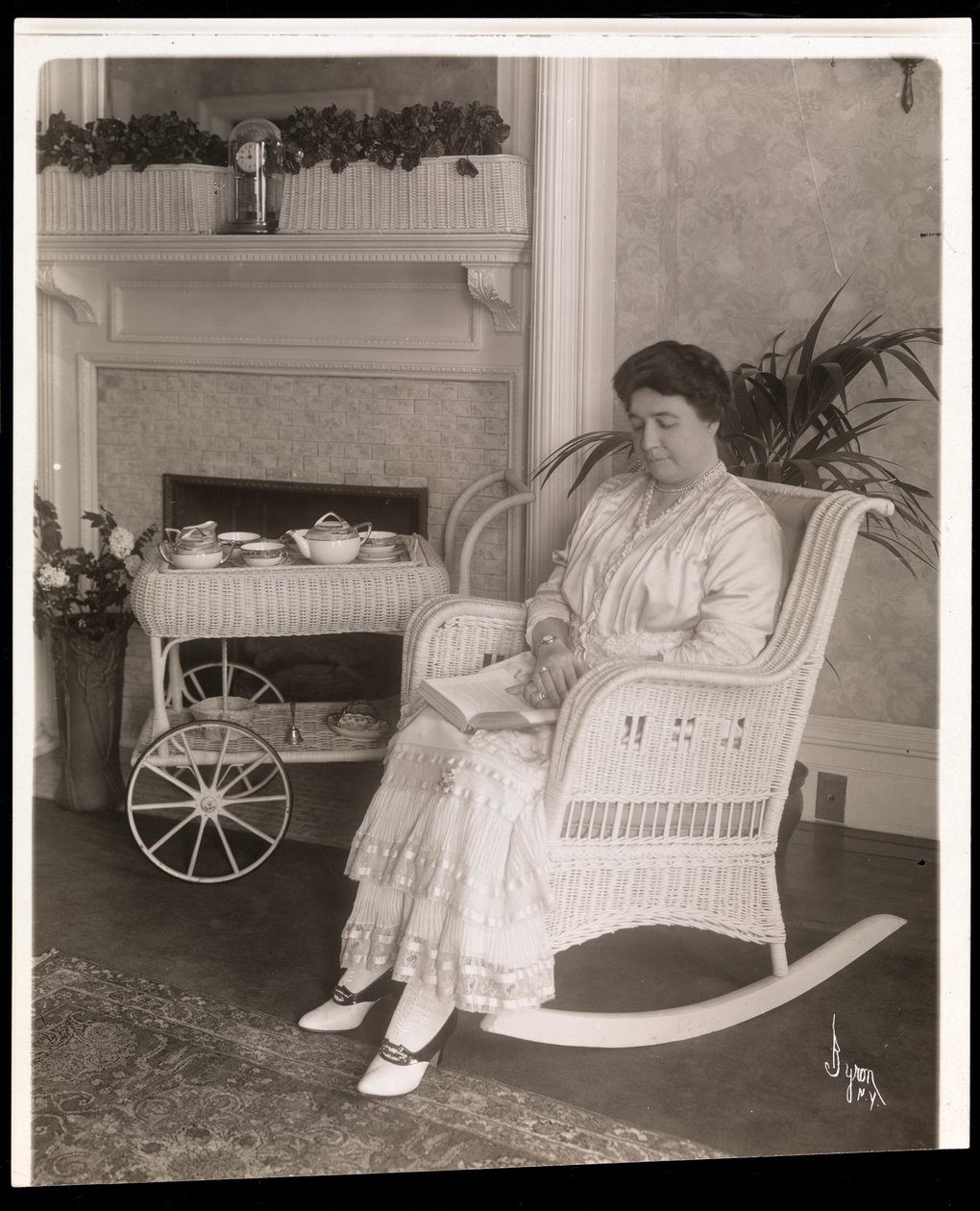 Mme Howard assise avec un livre dans un fauteuil à bascule chez elle au 200, 5e Avenue, New York, 1915-6 - Byron Company