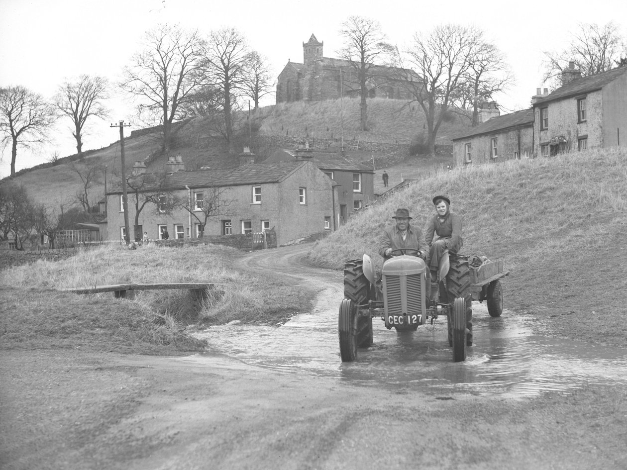 Un homme et une femme conduisant un tracteur descendent la route à travers un gué à Crosby Garret - Joseph Hardman
