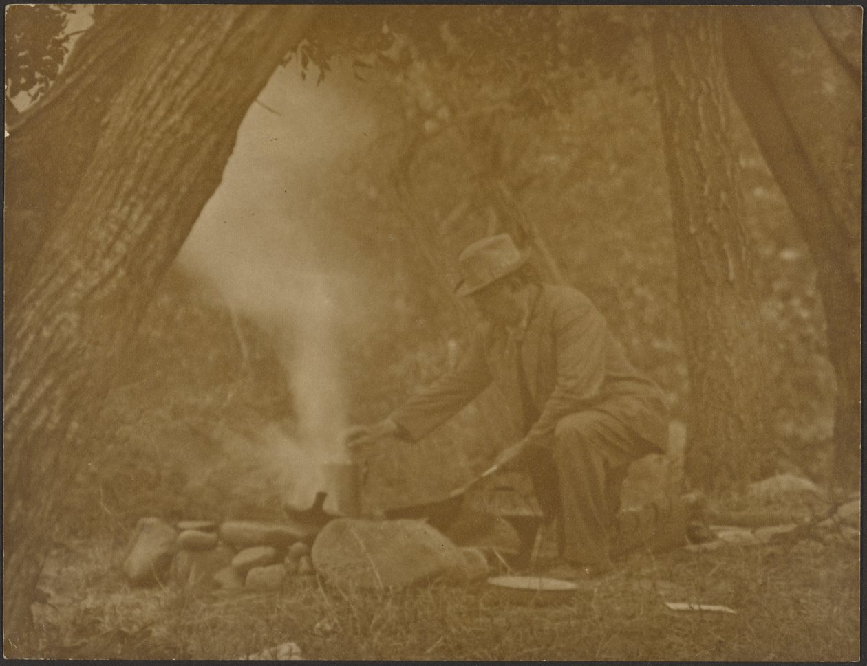 [Un homme en train de cuisiner sur un feu de camp dans les bois] - Louis Fleckenstein