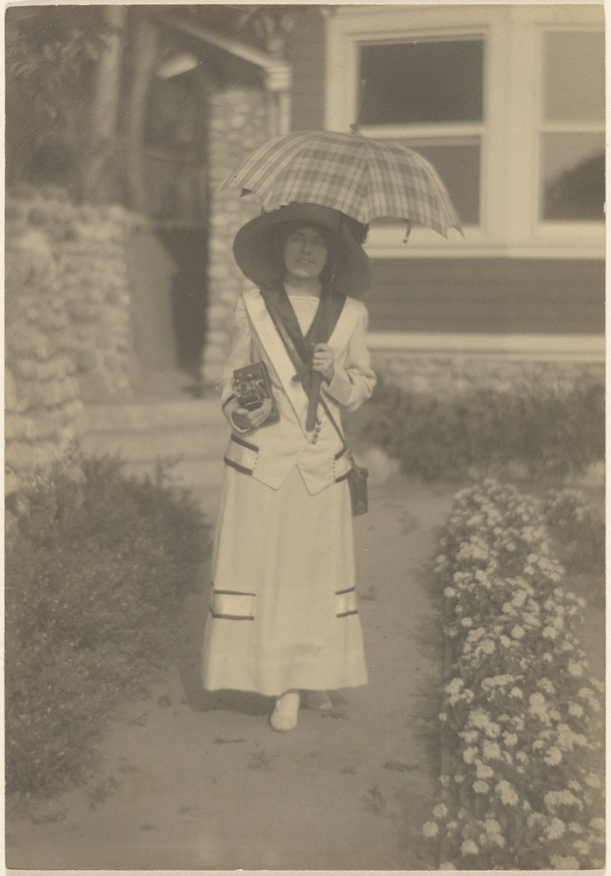 [Femme debout dans le jardin devant la maison, avec un appareil photo et un parapluie à carreaux] - Louis Fleckenstein