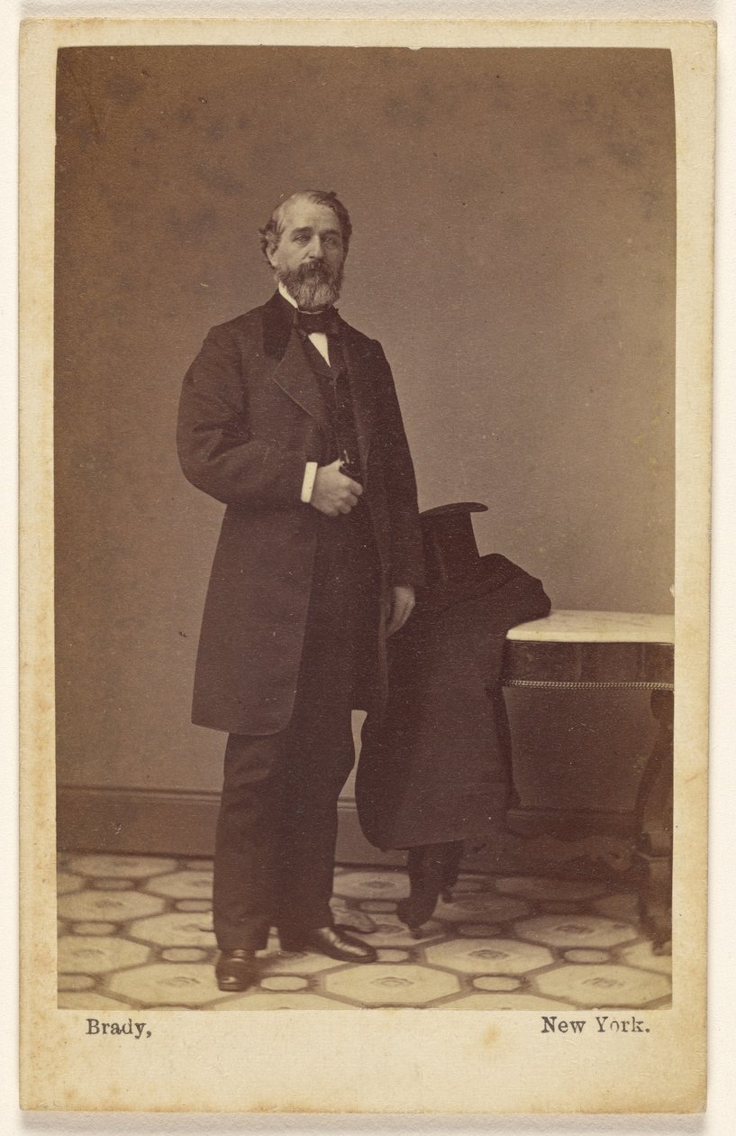 [Un homme barbu non identifié, debout ; un haut-de-forme et un manteau posés sur une table à proximité] - Mathew B. Brady
