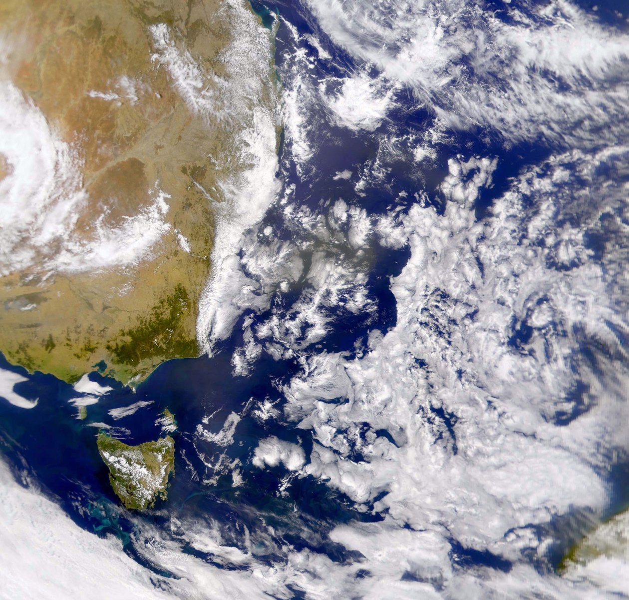 Photographie satellite de la mer de Tasman partiellement couverte de nuages. À gauche, une partie de l