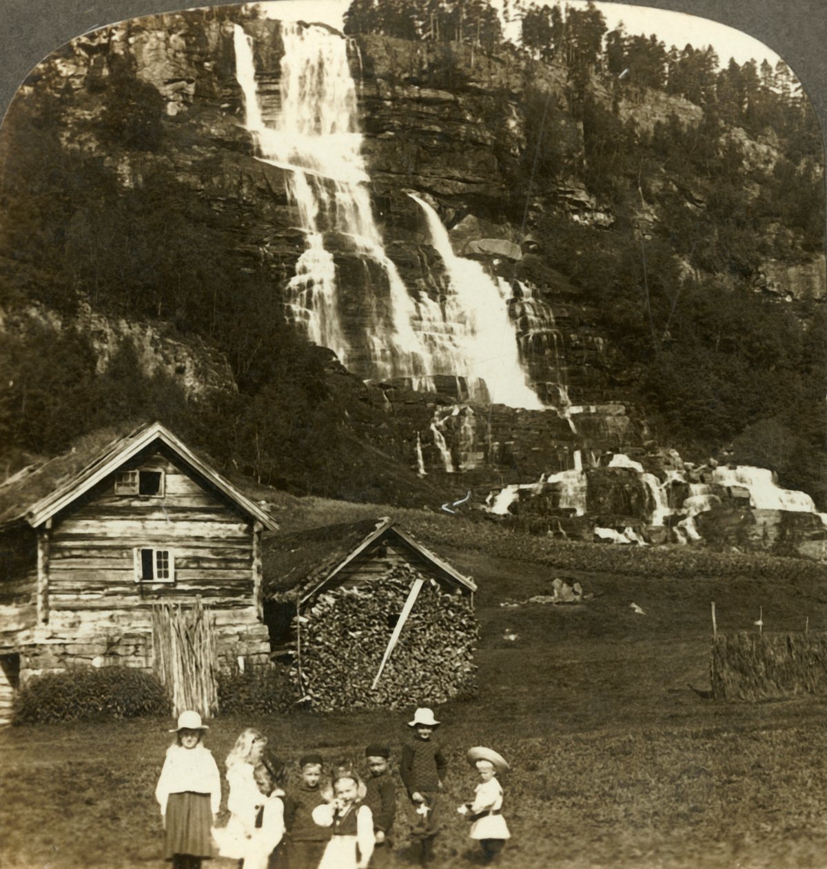 Enfants jouant dans un champ de fermier avec la cascade en terrasses de Tvinde, Vossevangen, Norvège, vers 1905 - Unbekannt
