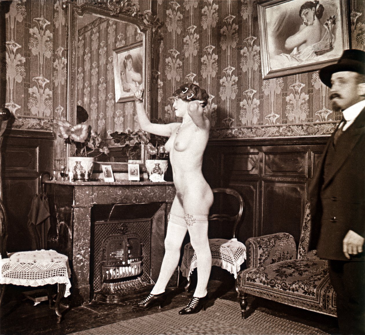 Photographie énigmatique montrant une jeune femme complètement nue (sauf ses chaussures et ses bas) recoiffant ses cheveux devant un miroir en présence d
