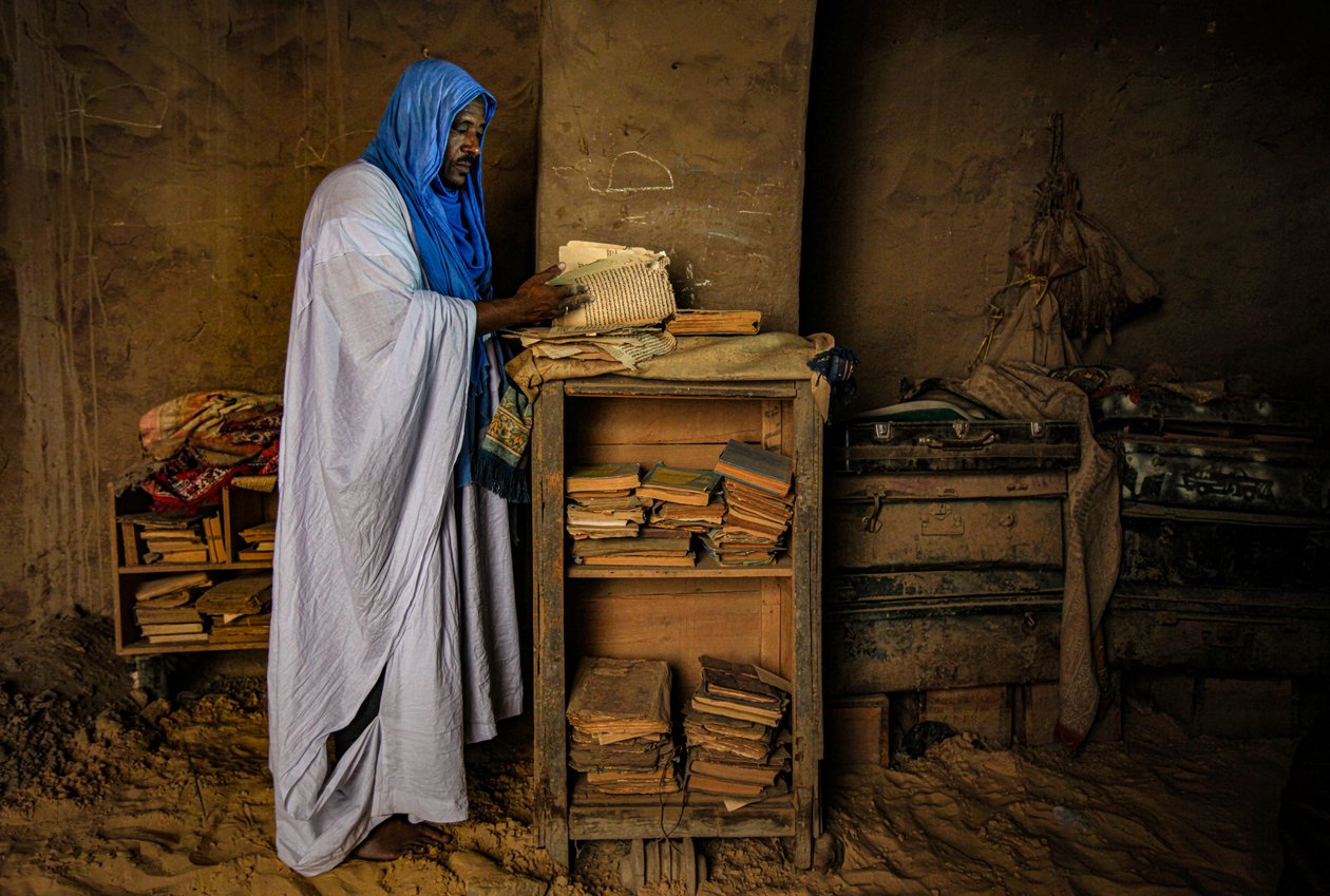 Homme feuilletant un manuscrit précieux dans sa maison sablonneuse, 2009 (photographie) - Unbekannter Künstler