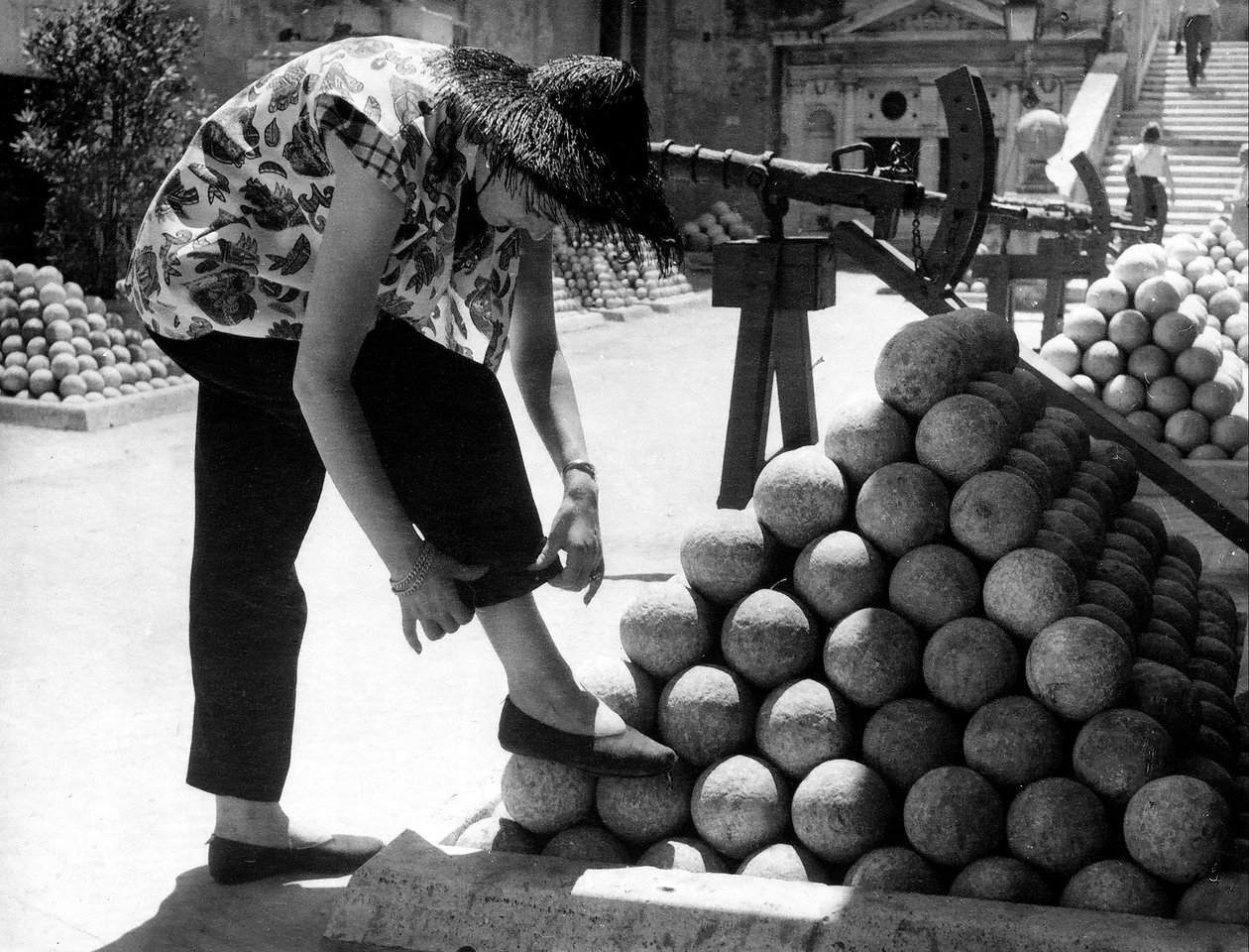 Une femme ajuste le revers de son pantalon en posant son pied sur une pile de boulets de canon dans l