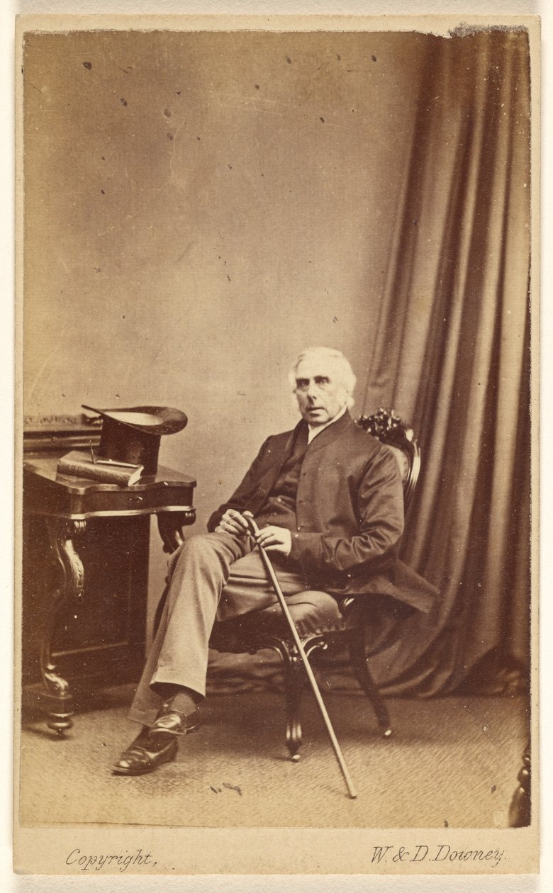 [Homme non identifié aux cheveux blancs, assis, tenant une canne, un chapeau haut de forme et un livre sur la table à gauche]. - W. and D. Downey