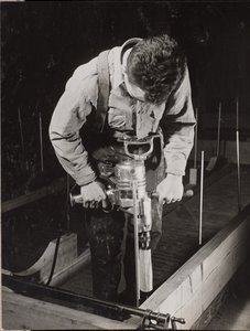 [Un homme utilise une machine portative pour travailler un morceau de bois].