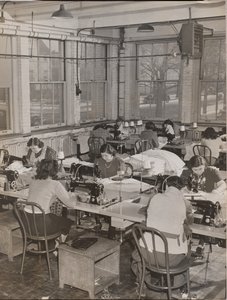 [Des femmes assises à des bureaux travaillent sur des machines à coudre]. - Arnold Eagle