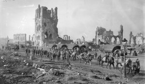 Une section de mitrailleuses australienne non identifiée avec des chevaux de bât passant devant les ruines de la Halle aux Draps. Notez plusieurs camions à moteur garés en arrière-plan, 19 octobre 1917
