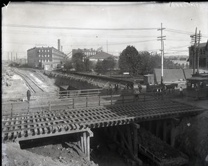 Photographie horizontale en noir et blanc montrant un pont en bois et des voies de tramway sur des voies ferrées partiellement construites. Un tramway marqué Chouteau 2137 commence à traverser le pont à l