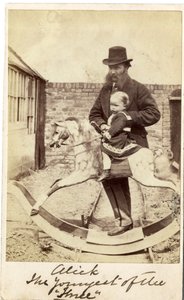 Jeune fille sur un cheval à bascule dans le jardin, son père à côté - English Photographer