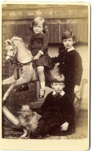 Jeune fille sur un cheval à bascule avec un garçon debout et un garçon assis avec un chien - English School