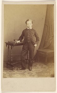 [Petit garçon non identifié en costume, debout devant une table sur laquelle sont posés des livres]. - Joseph Brown