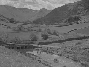 Vue sur un pont, un ruisseau, des champs et des montagnes.