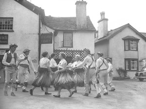 Hommes et femmes dansant à Hawkshead avec une enseigne pour le "15 Century Café" derrière et des commissaires-priseurs - Joseph Hardman
