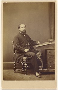 [Homme barbu non identifié assis à un pupitre, de profil 3/4].