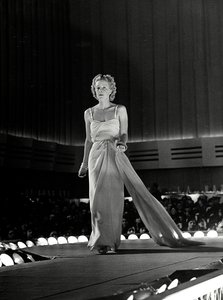 Mannequin photographié sur un podium en robe de soirée avec des bretelles en strass ; l
