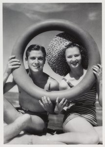 Homme et femme regardant à travers une bouée sur la plage, vers 1935