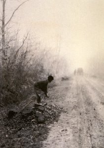 Une route de campagne enveloppée de brumes matinales. Au premier plan, un homme fend des pierres - Unbekannter Künstler