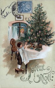 Carte de vœux de Noël : un enfant devant un sapin de Noël pose sur une table, observé par un ange à la fenêtre - Carte postale datée de 1905