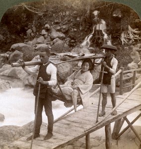 Femme japonaise dans une chaise de montagne yamakago traversant la rivière torrentielle Daiya près de Nikko, Japon - Underwood and Underwood
