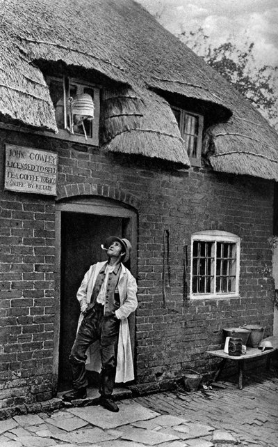 Un homme fumant une pipe devant un magasin, Worcestershire - A. W. Cutler