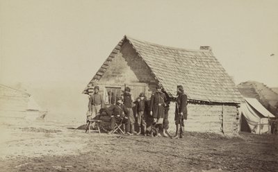 Un groupe de soldats et deux jeunes hommes, dont un afro-américain, devant des quartiers en cabane en rondins, 1861-65 - American Photographer