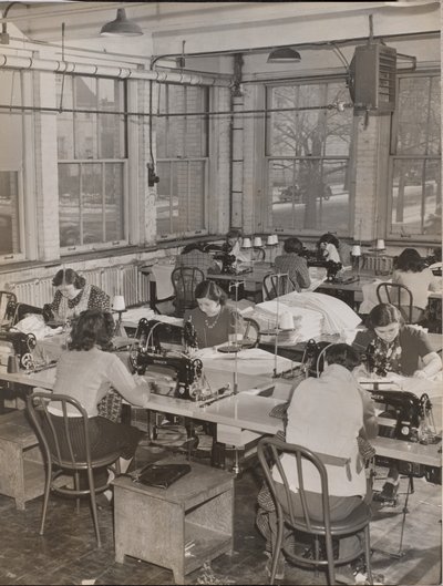 [Des femmes assises à des bureaux travaillent sur des machines à coudre]. - Arnold Eagle
