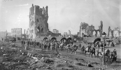 Une section de mitrailleuses australienne non identifiée avec des chevaux de bât passant devant les ruines de la Halle aux Draps. Notez plusieurs camions à moteur garés en arrière-plan, 19 octobre 1917 - Australian Photographer