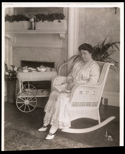 Mme Howard assise avec un livre dans un fauteuil à bascule chez elle au 200, 5e Avenue, New York, 1915-6 - Byron Company