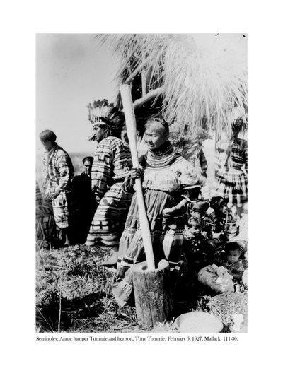Annie Jumper Tommie utilisant un mortier et un pilon pour faire de la farine de maïs, et son fils, Tony Tommie, portant un bonnet de plumes d