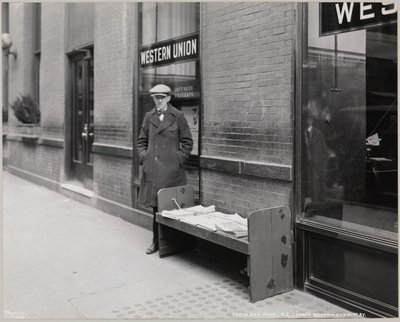 Le marchand de journaux aveugle, Frederick Rode, et le coin sud-est de Broadway et de la 41e Rue. Une enseigne Western Union est visible dans la fenêtre derrière M. Rode - Company Byron