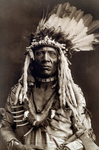 Queue de belette (Apohsuyis). Portrait du chef indien de la tribu Piegan portant la célèbre coiffe en plumes d