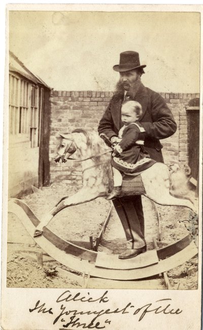 Jeune fille sur un cheval à bascule dans le jardin, son père à côté - English Photographer