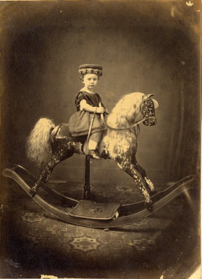 Jeune fille assise sur un cheval à bascule tacheté - English Photographer