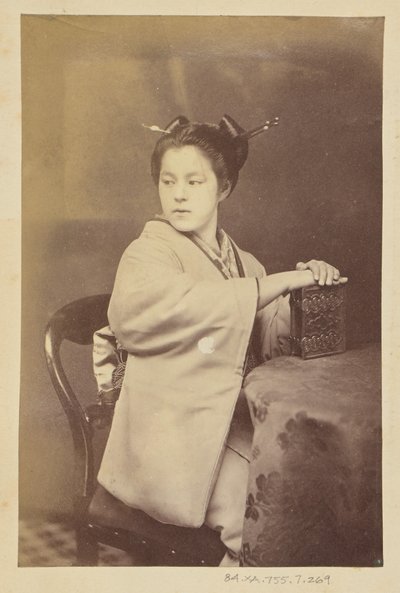 [Femme japonaise assise tenant un album de cartes-de-visite à une table]. - Felice Beato