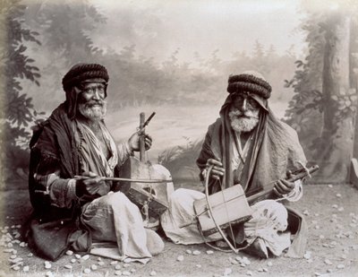 Portrait de deux musiciens arabes en tenue ethnique modeste. Les hommes âgés posent dans le studio, assis par terre. Derrière eux, un décor de paysage boisé - Félix Bonfils