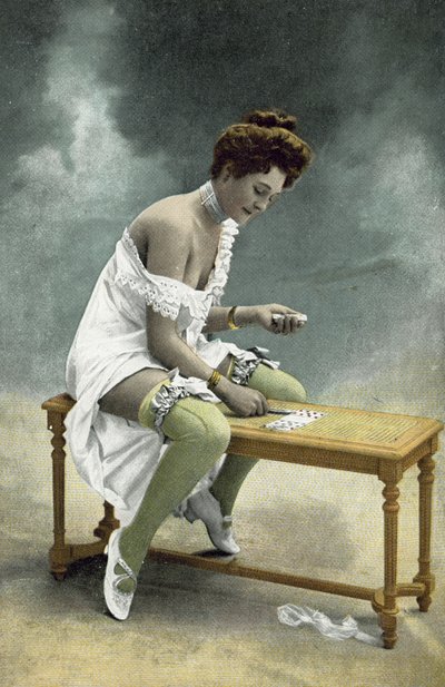 Fille avec des bas et un sein exposés jouant à la patience sur un tabouret en bois - French Photographer