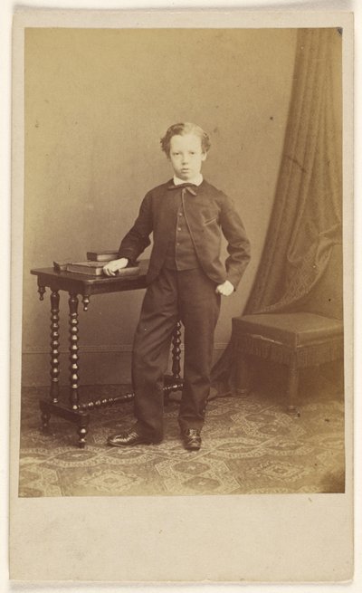 [Petit garçon non identifié en costume, debout devant une table sur laquelle sont posés des livres]. - Joseph Brown