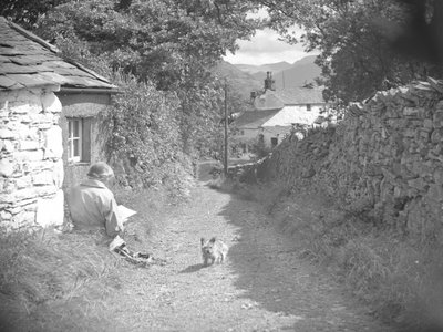 Une femme assise en train de lire avec un chien dans une ruelle - Joseph Hardman