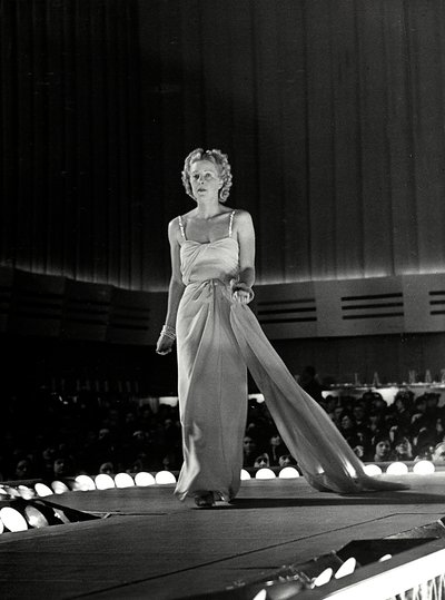 Mannequin photographié sur un podium en robe de soirée avec des bretelles en strass ; l
