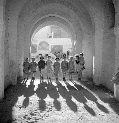 Enfants européens en uniforme scolaire sous une arche avec des ombres. - Maynard Owen Williams