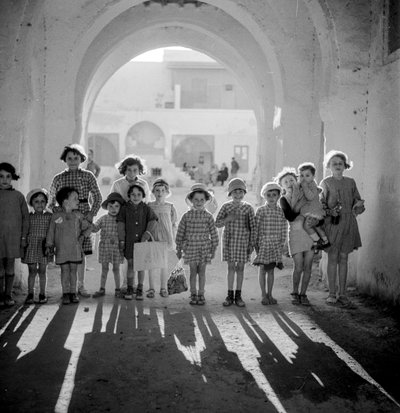 Enfants européens en uniforme scolaire sous une arche avec des ombres. - Maynard Owen Williams