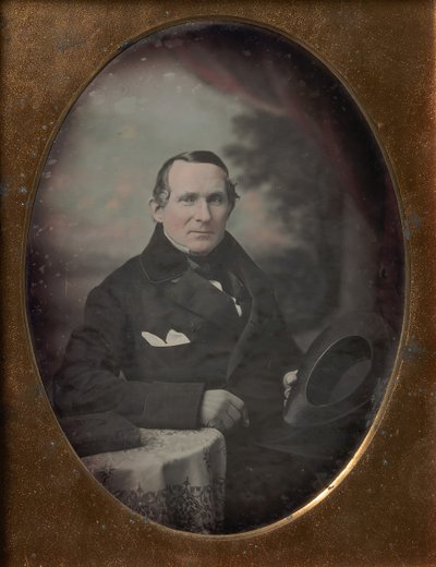 Homme portant un manteau et des gants, tenant un chapeau, assis devant un décor extérieur peint, années 1840 - Samuel Broadbent Jr..