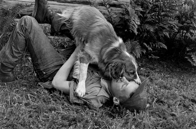 Jeune homme jouant avec son chien devant leur cabane en rondins à Palmer, Alaska - Ted Spiegel